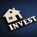 Word Invest and model of home from wood. Real Estate Investment concept.